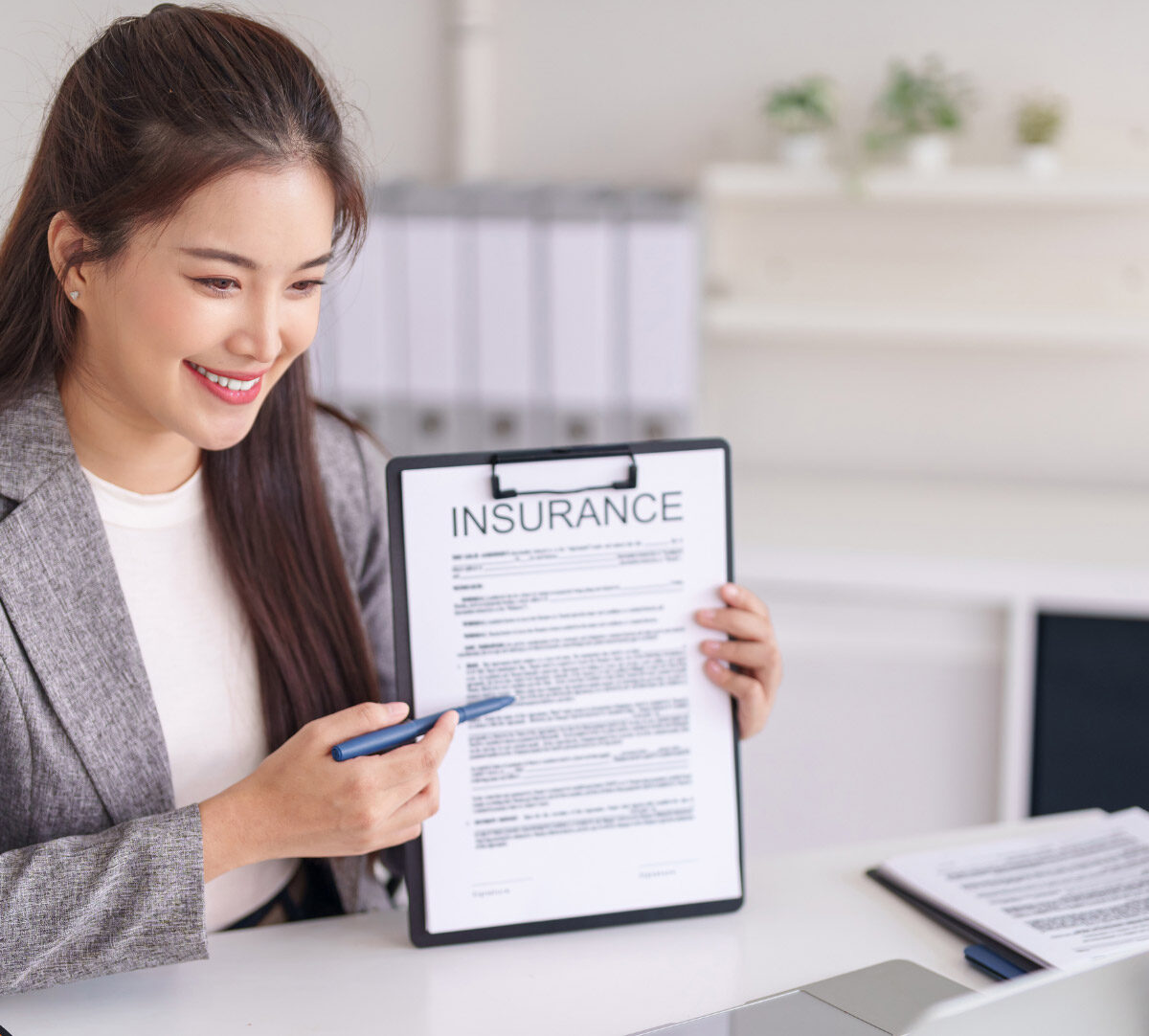 smiling woman holding clipboard in front of laptop screen